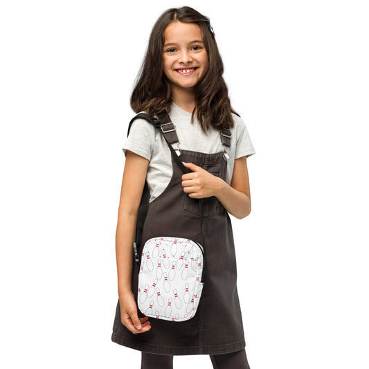 White crossbody bag with pink bowling pin pattern worn over black pinafore dress and white t-shirt.