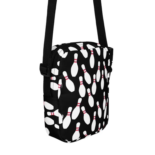 Black crossbody bag with white bowling pin pattern and adjustable strap.