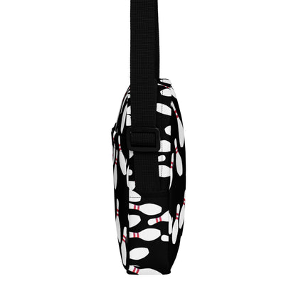 Slim black crossbody bag with white bowling pin pattern and adjustable strap.