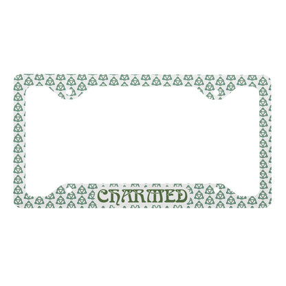 White metal license plate frame with green Celtic knot pattern and "CHARMED" lettering at bottom center.