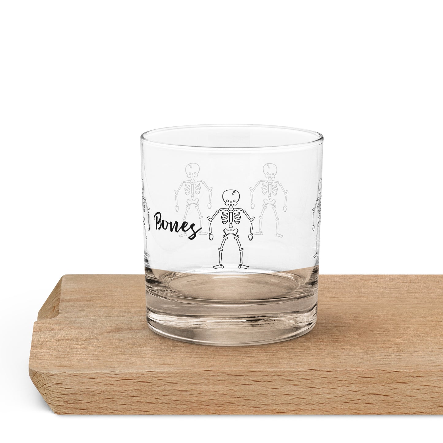 Clear glass tumbler with a black skeleton graphic and the word "Bones" on the side, resting on a wooden surface.